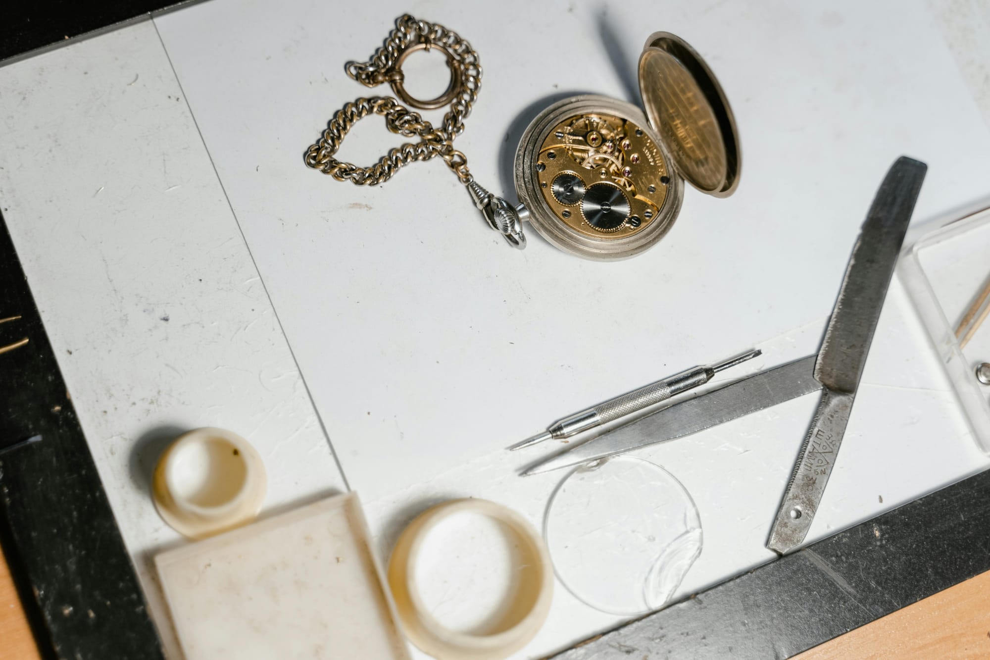 Opened pocket watch with case back removed, showing the movement alongside repair tools on a workbench